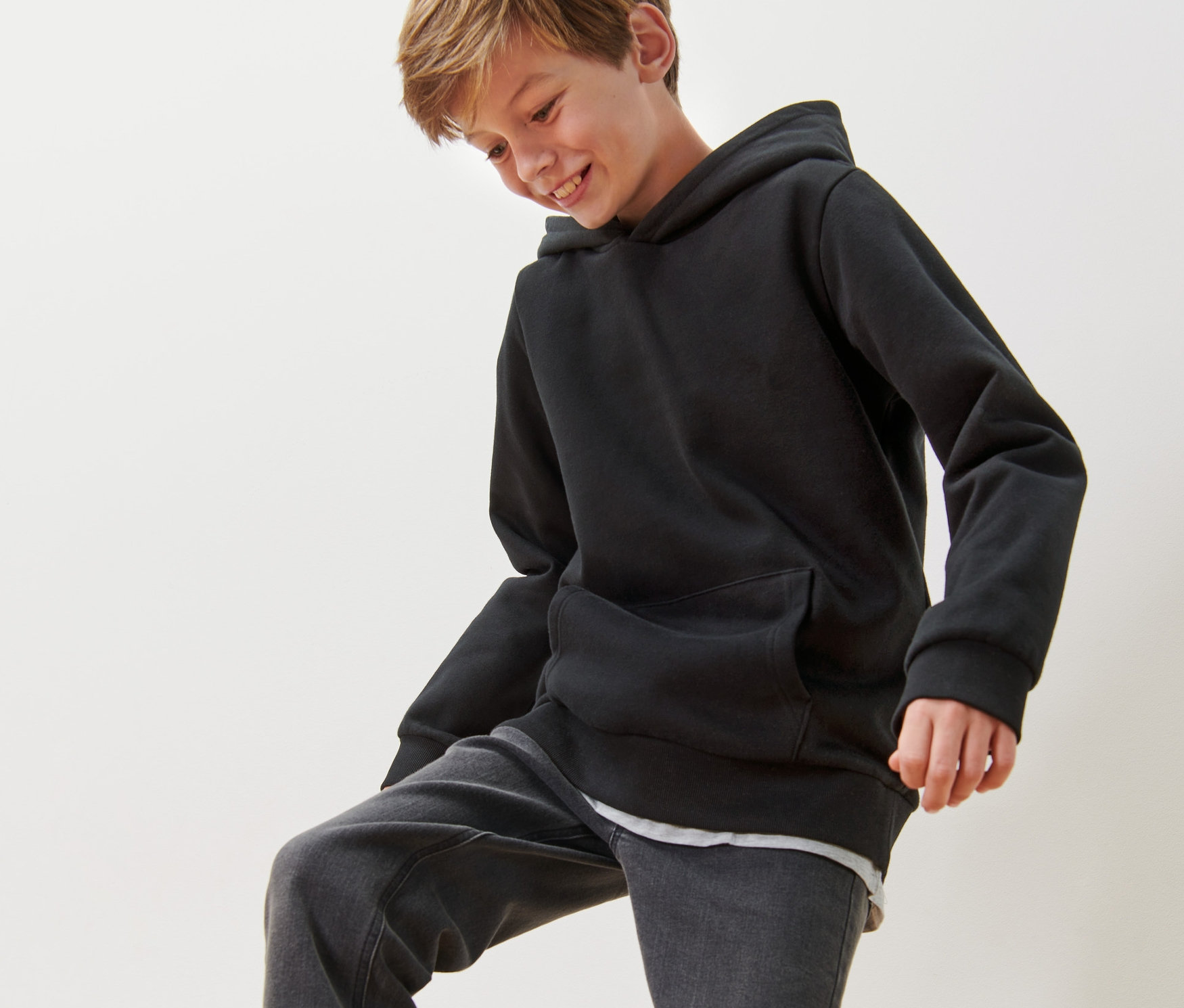 Ein Junge trägt einen Kinder-Sweat-Hoodie und Jeans.
