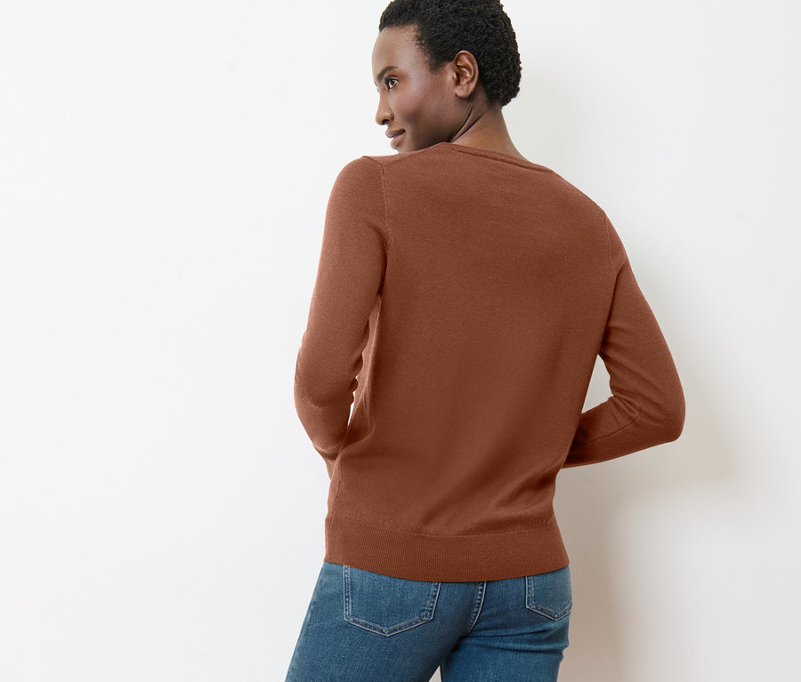 Frau blickt über die Schulter und trägt einen cognacfarbenen Merino-Feinstrickpullover.