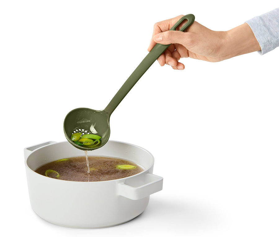 Eine Hand hält eine grüne Multifunktions-Schöpfkelle über einen Topf mit Suppe.