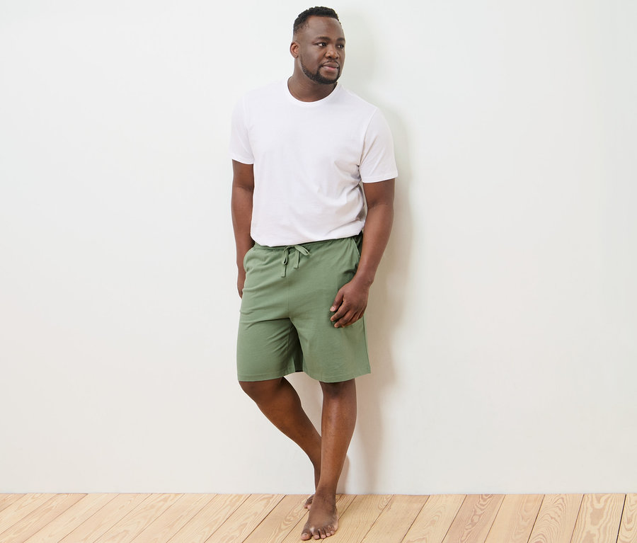 Mann in weißem T-Shirt und Relaxshorts steht an der Wand.