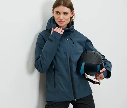 Frau posiert in marineblauer Skijacke und hält einen Helm.