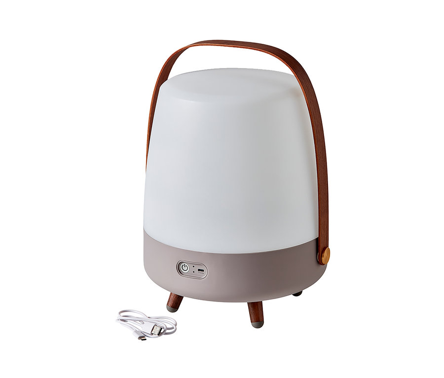 Eine weiße LED-Lampe mit braunem Griff und grauem Sockel steht auf drei Beinen neben einem weißen Ladekabel. Zu sehen ist ein Design LED-Licht mit Bluetooth®-Lautsprecher.