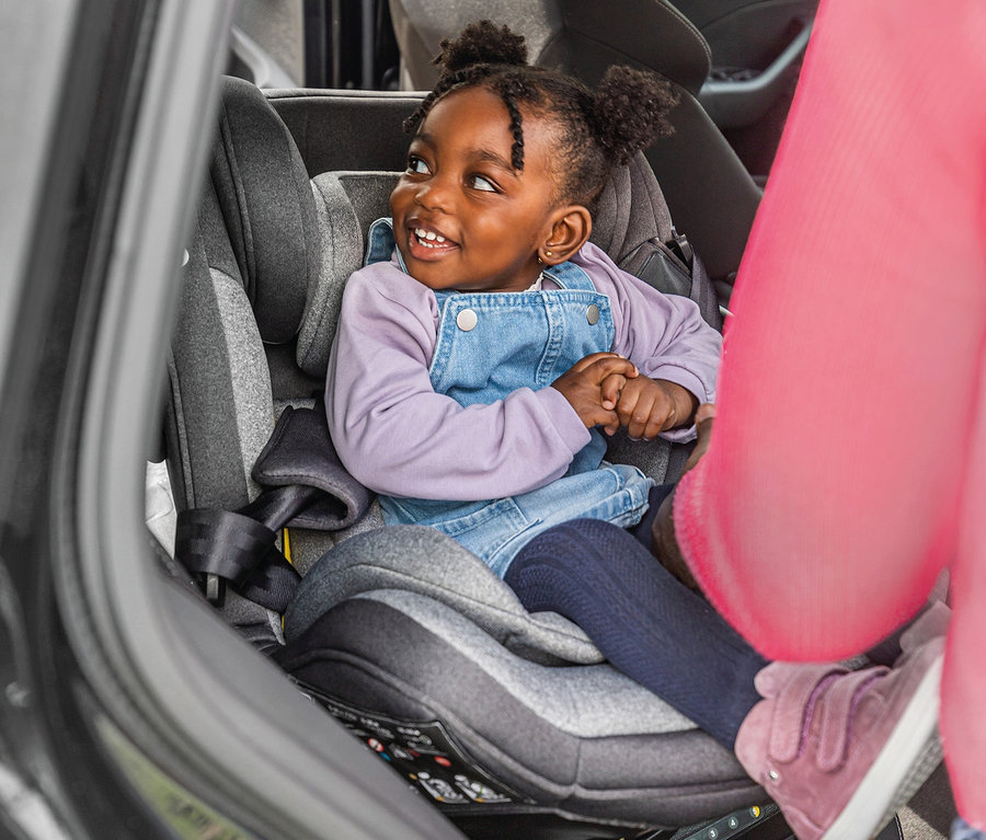 Lächelndes kleines Mädchen sitzt im Osann Kindersitz Swift360 S in einem Auto.