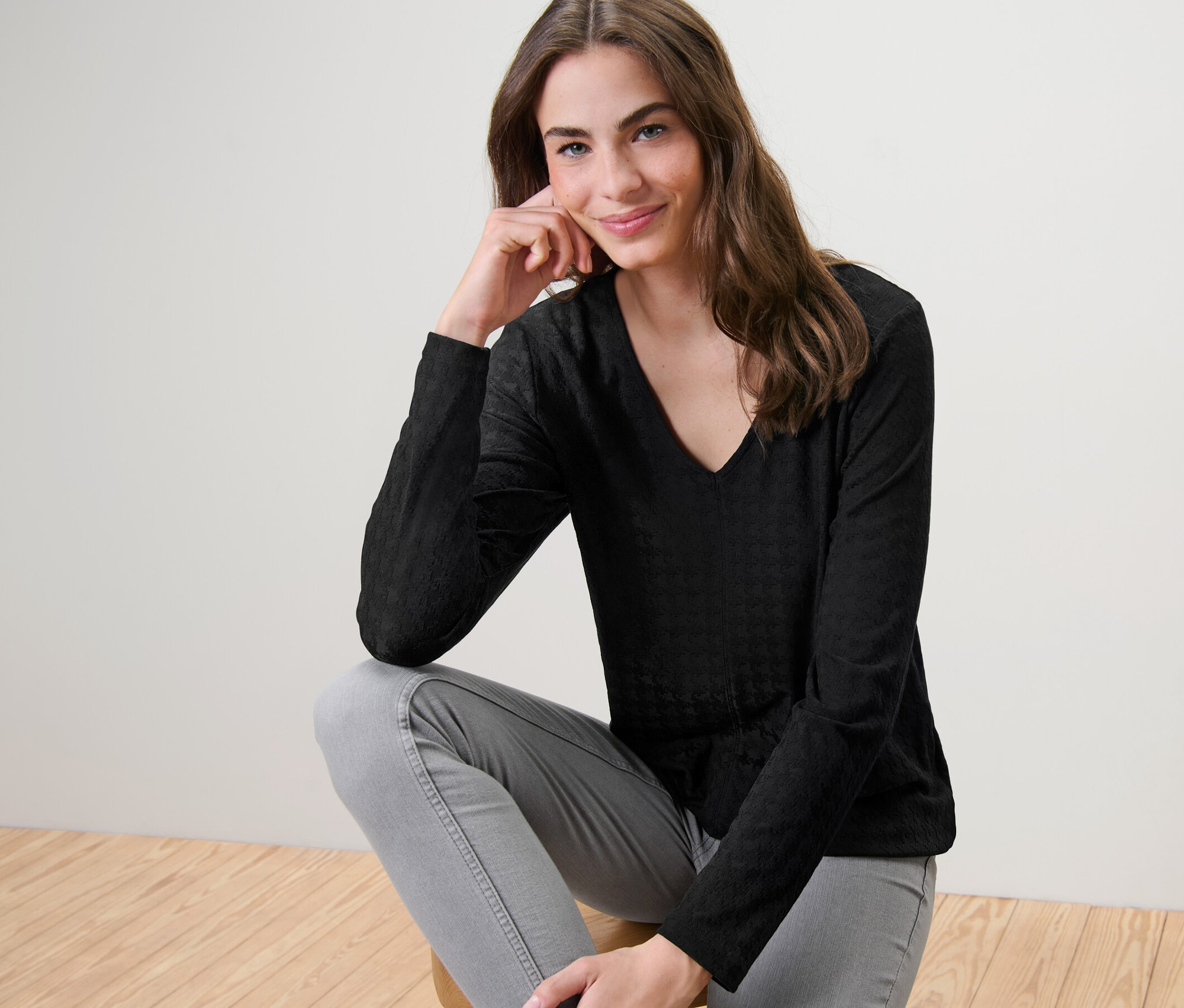 Frau sitzt auf einem Hocker und trägt ein strukturiertes Langarmshirt, schwarz.