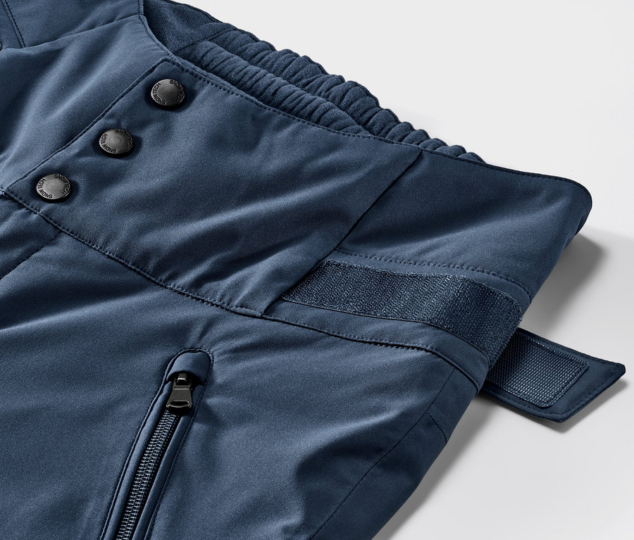 Detailaufnahme einer blauen High-Waist-Skihose. Knopf-, Reißverschluss- und Klettverschlussdetails.