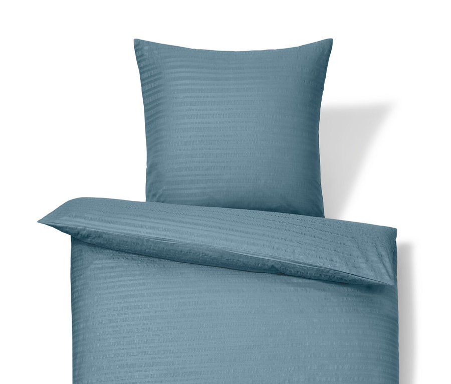 Blaue Seersucker-Bettwäsche in Normalgröße und blaue Seersucker-Bettwäsche in Übergröße liegen übereinander.