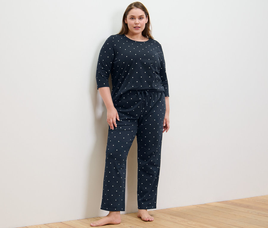 Eine Frau steht und trägt einen Pyjama mit Punkten.