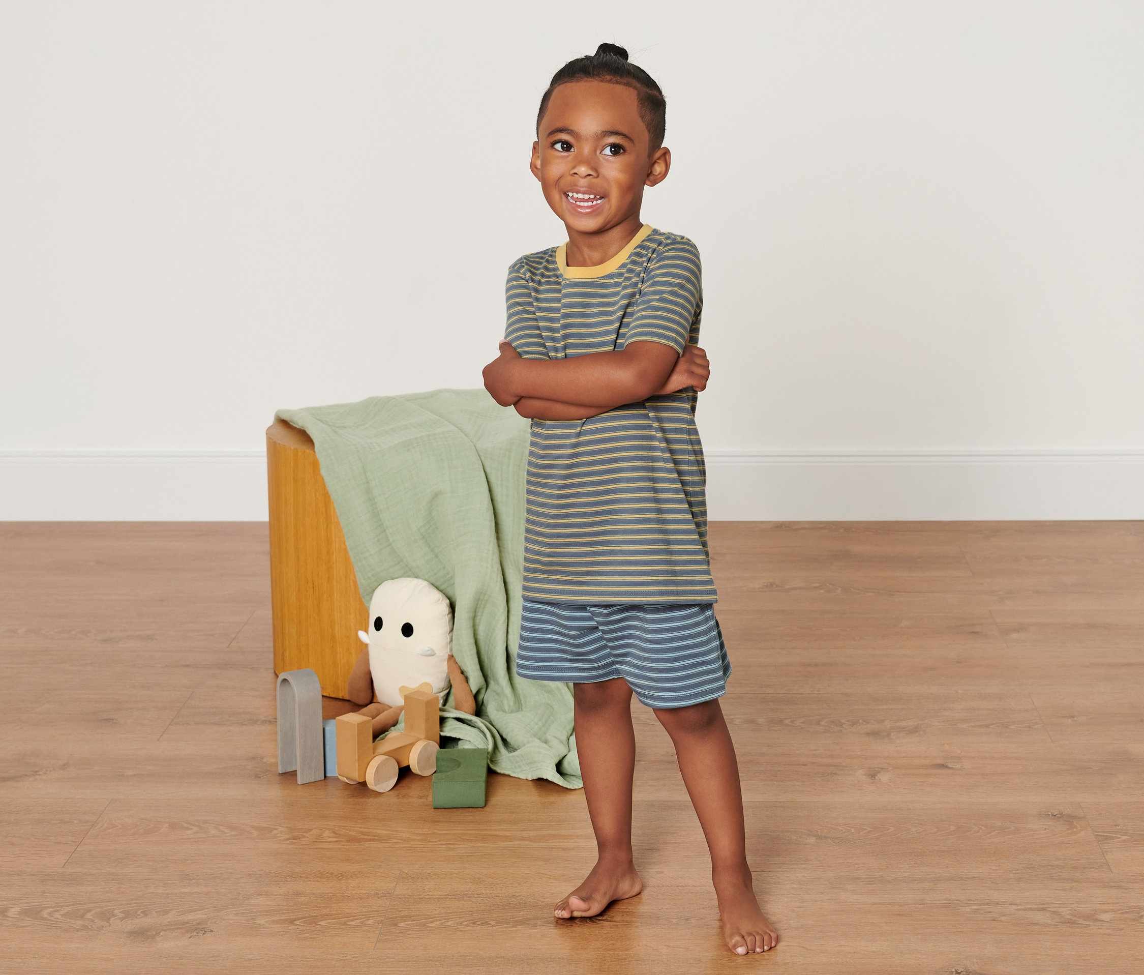 Junge steht mit verschränkten Armen da und trägt einen gelb-grau gestreiften Schlafanzug.