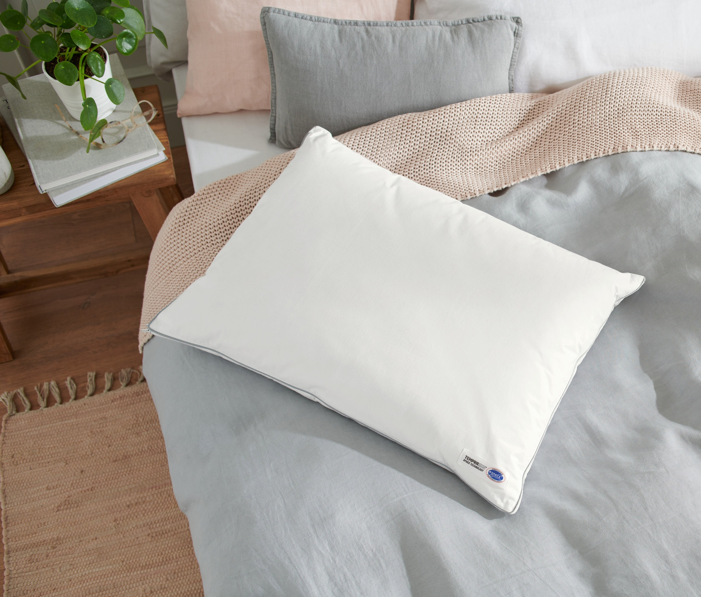 Weißes Temprakon Ergonomic Kissen liegt auf einem Bett mit grauer Bettwäsche.