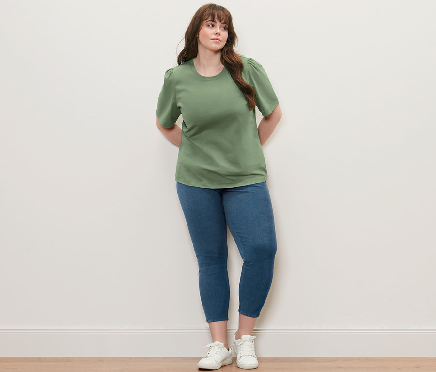 Frau posiert in grünem Shirt mit Raffung und Jeggings.