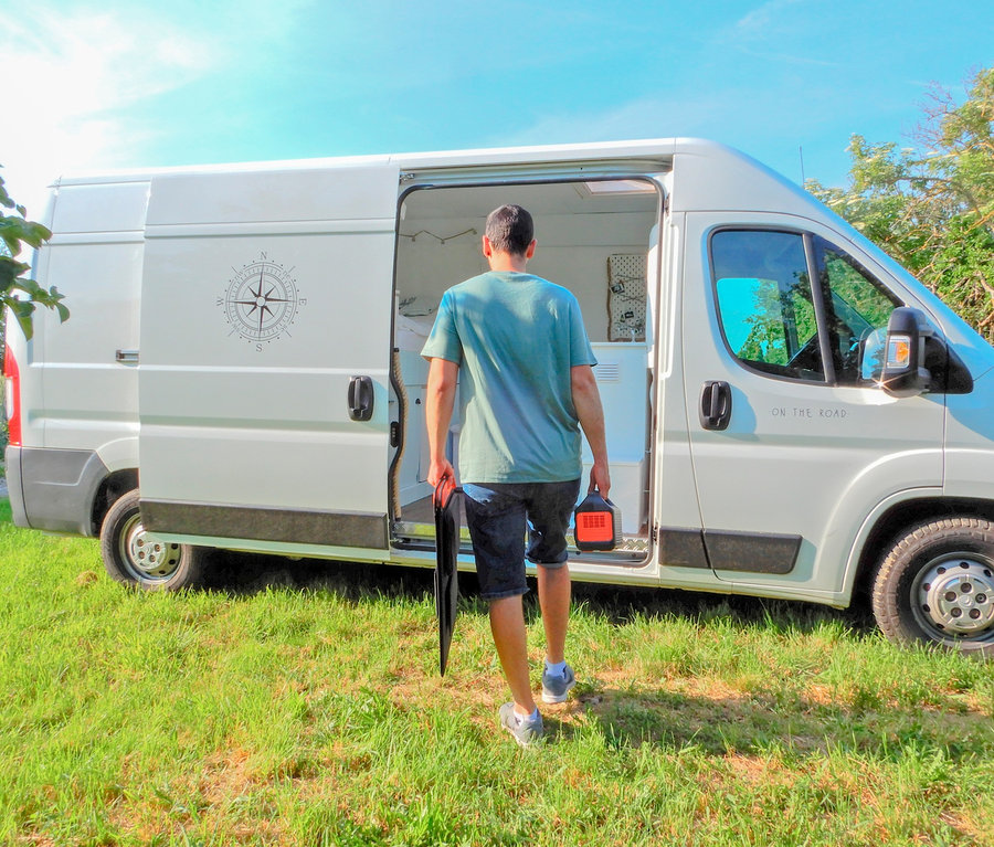 Mann geht in einen weißen Lieferwagen mit offener Tür und hält ein Solarpanel und einen Jackery Explorer 240 in der Hand.