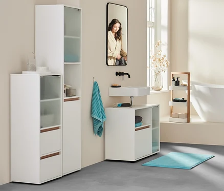 Im Badezimmer steht eine Frau im Bademantel an der Badewanne. Im Vordergrund Sideboard, Bad, extragroßes Badetuch in Anthrazit und zwei aqua Handtücher.
