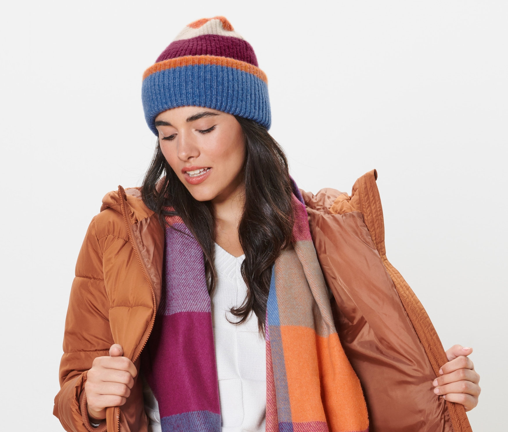 Frau in brauner Jacke richtet ihre Strickmütze und trägt einen Schal.