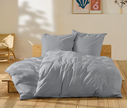 Graue Perkal-Bettwäsche in Normal- und Übergröße auf einem Bett.