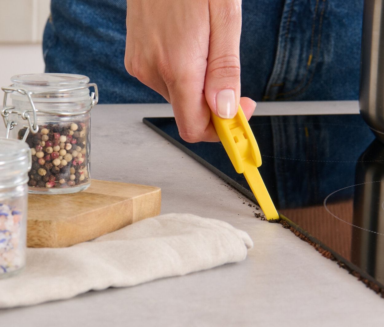 Frau reinigt den Rand eines Glaskeramikkochfelds mit einer 3-in-1-Reinigungsbürste.