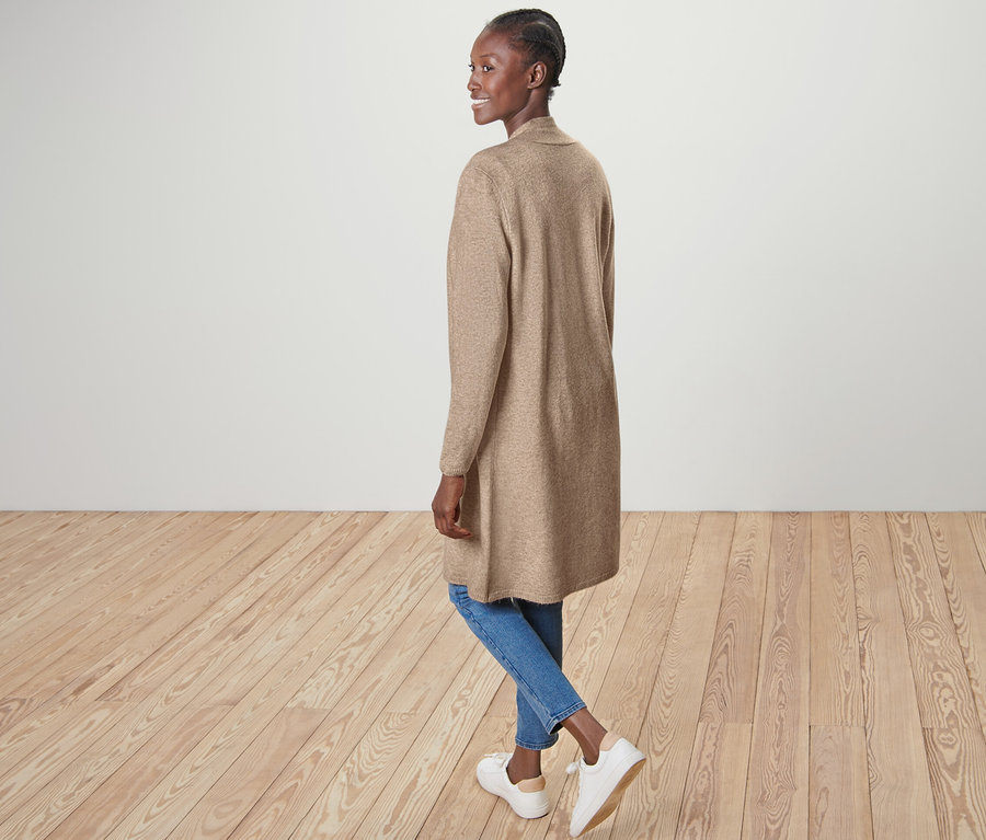 Frau posiert in offenem Longcardigan, blauen Jeans und weißen Schuhen.