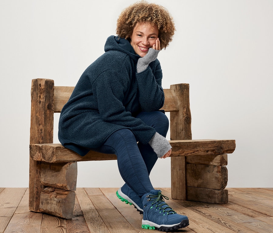 Frau sitzt auf einer Holzbank und trägt einen Oversized Teddy-Mantel und Sporttights.
