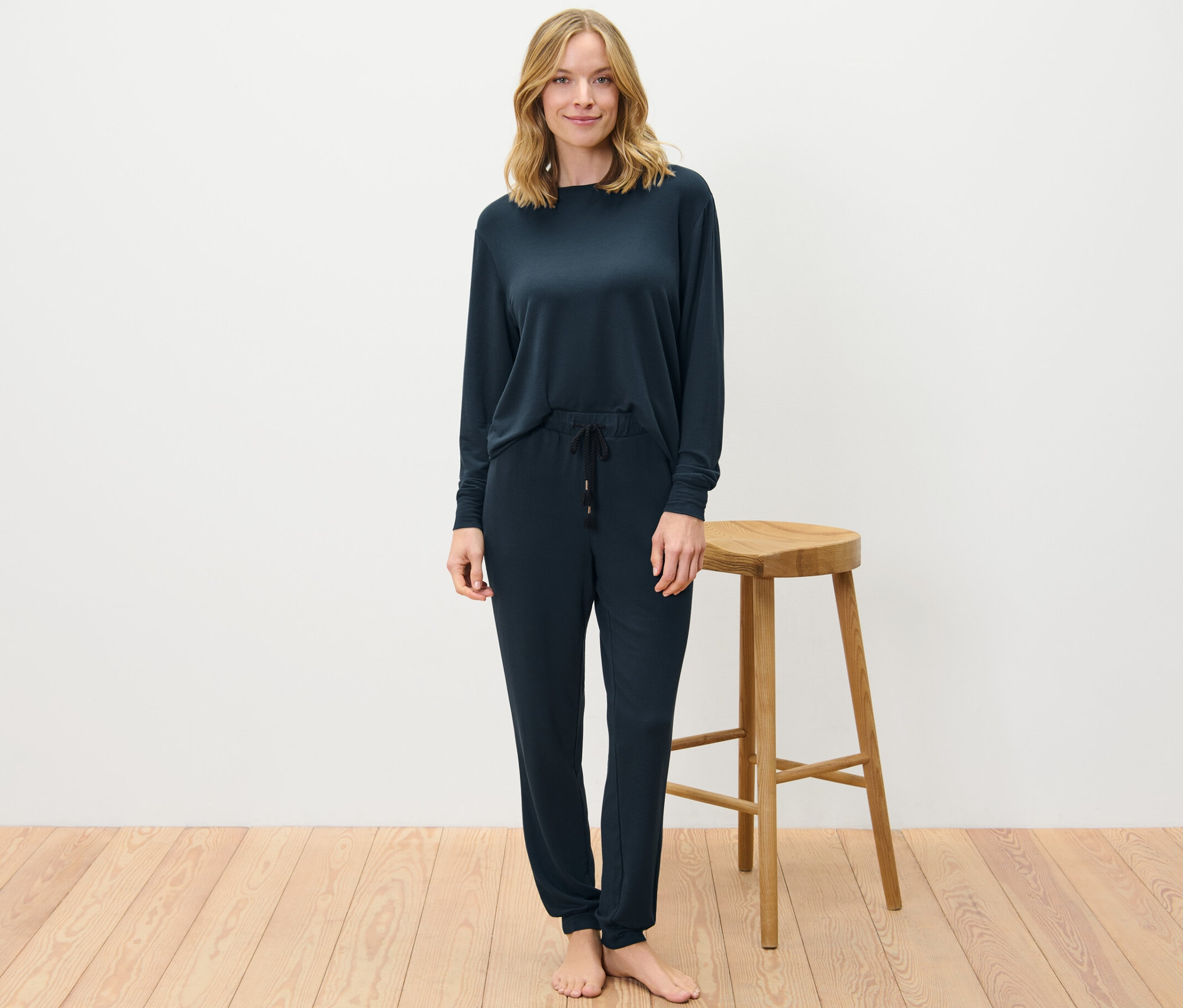 Blonde Frau steht und trägt einen dunkelblauen Hausanzug.