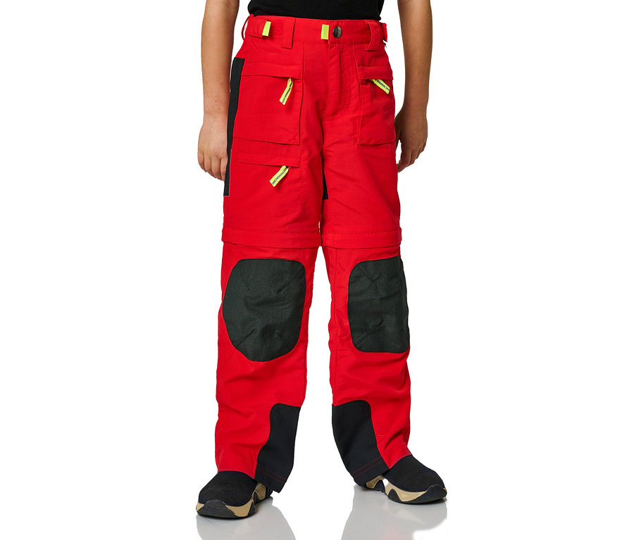 Ein Junge trägt eine rote Jako-O Zipp-off-Hose mit schwarzen Knieflicken und schwarzen Einsätzen an den Beinenden.