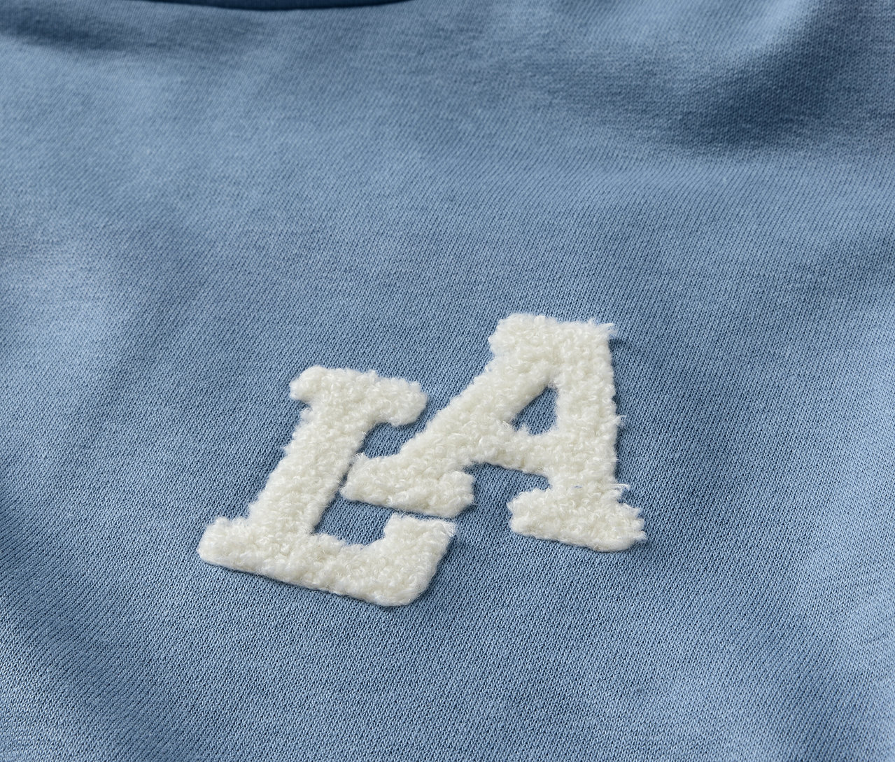 Detailansicht eines hellblauen Kinder-Sweat-Hoodies mit weißem LA-Schriftzug.