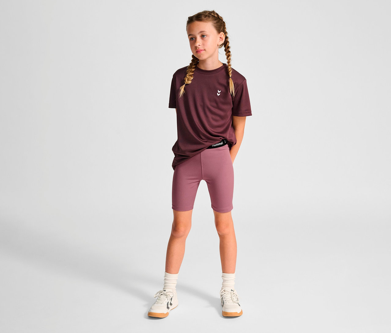 Mädchen steht in einem lila T-Shirt und HUMMEL HMLJR Pulse MW Short Tight.