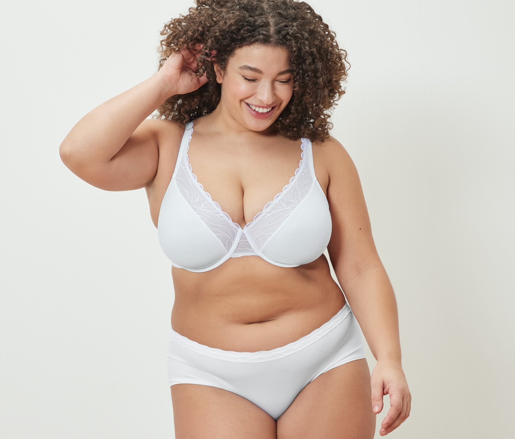 Lächelnde Frau berührt ihre Haare und trägt einen weißen Bügel-BH und Slips.