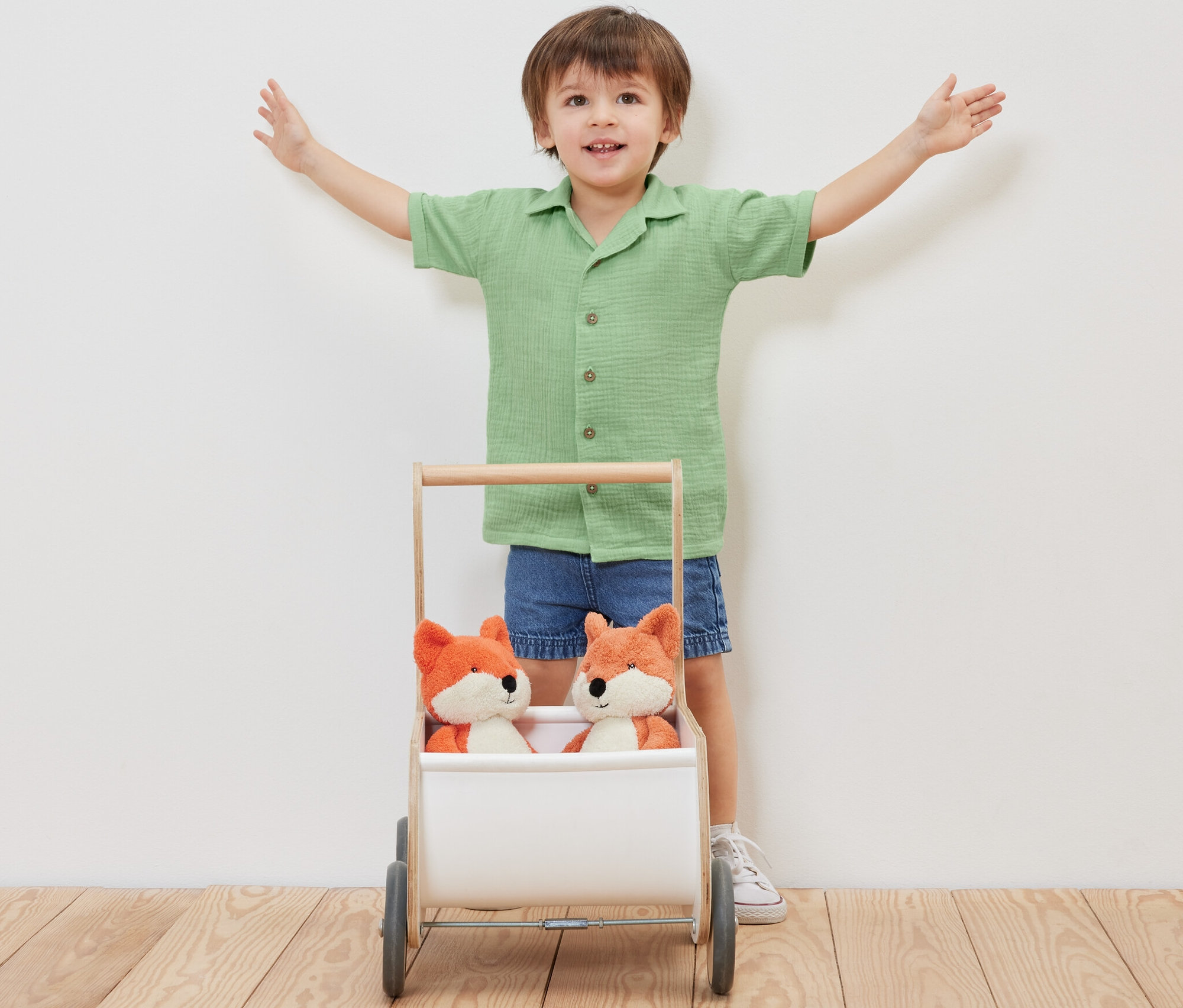 Junge steht mit ausgestreckten Armen hinter einem Wagen mit zwei Plüschfüchsen, trägt ein Kinder-Musselin-Hemd mit Kragen.