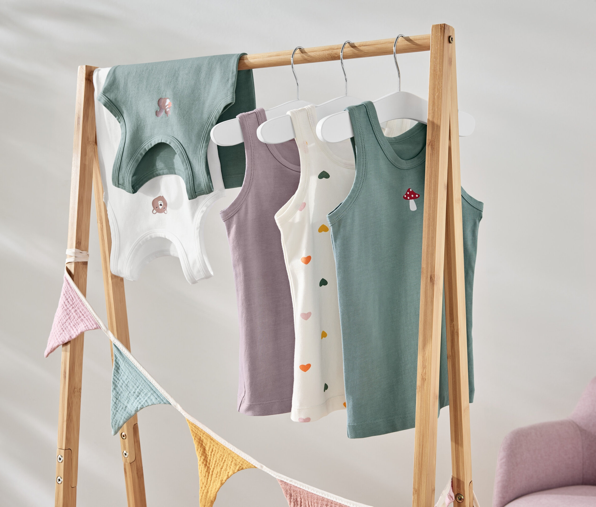 Auf einem Holzständer hängen bunte Kinder Tanktops mit verschiedenen Motiven.