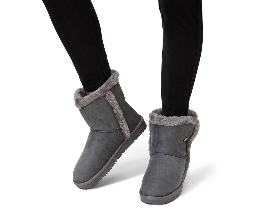 Beine in schwarzen Jeans, die graue Stiefeletten mit Pelzfutter tragen.