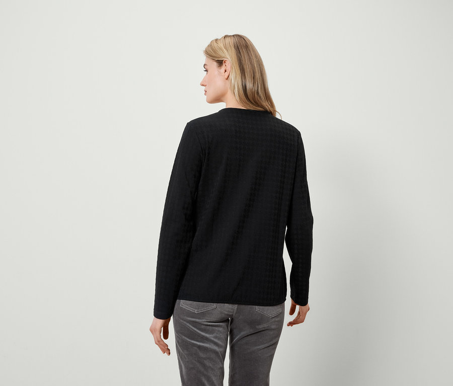 Frau schaut über die Schulter nach links, trägt ein schwarzes Langarmshirt und graue Hosen.