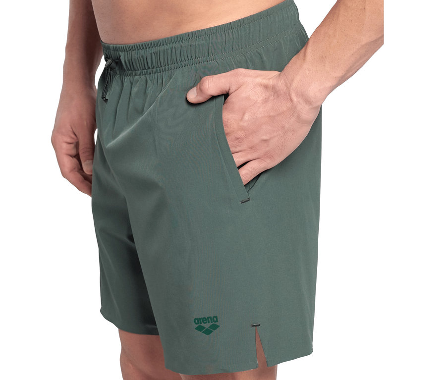 Mann trägt grüne arena Evo Badeshorts, mit der Hand in der Tasche.