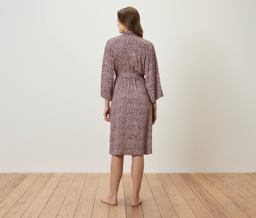 Frau steht mit dem Rücken zur Kamera und trägt einen rosa bedruckten Bademantel.