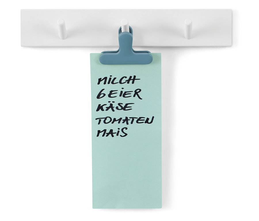Einkaufsliste mit blauem Clip an weißer Garderobe befestigt.