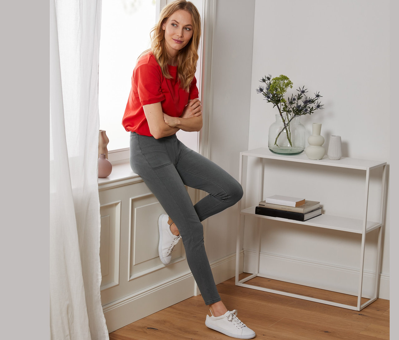 Frau sitzt im grauen Jeggings auf dem Fensterbrett.