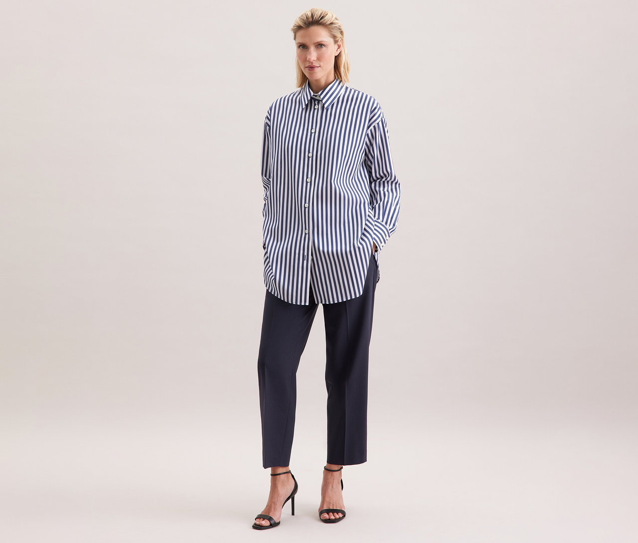 Frau trägt eine gestreifte Seidensticker Oversize Longbluse, kombiniert mit dunklen Hosen und schwarzen High Heels.