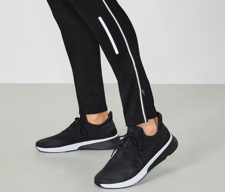 Schwarz-weiße Turnschuhe und schwarze Hosen mit reflektierenden Details.