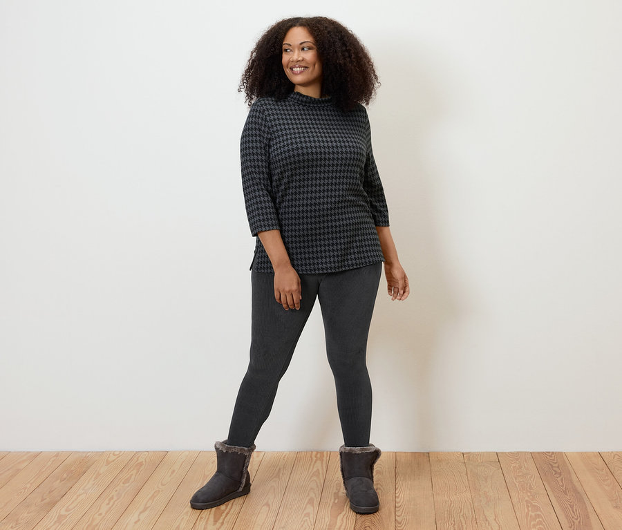Frau posiert in schwarzen Cord-Leggings, gemustertem Oberteil und Stiefeln.