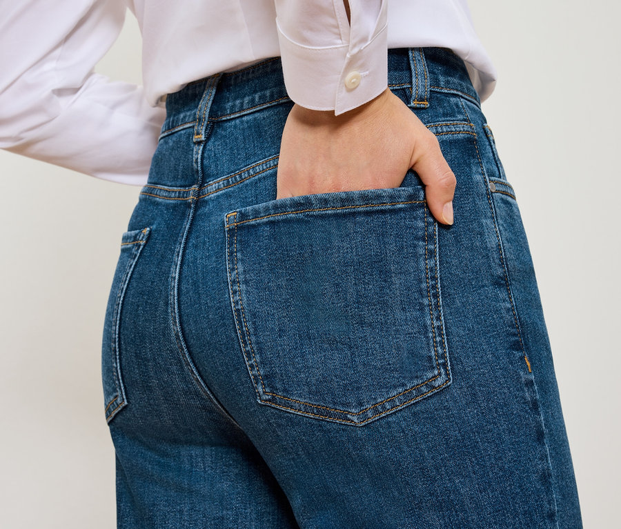 Rückansicht einer Frau mit Hand in der Tasche von blauen Mom Jeans – Fit »Nyla«.