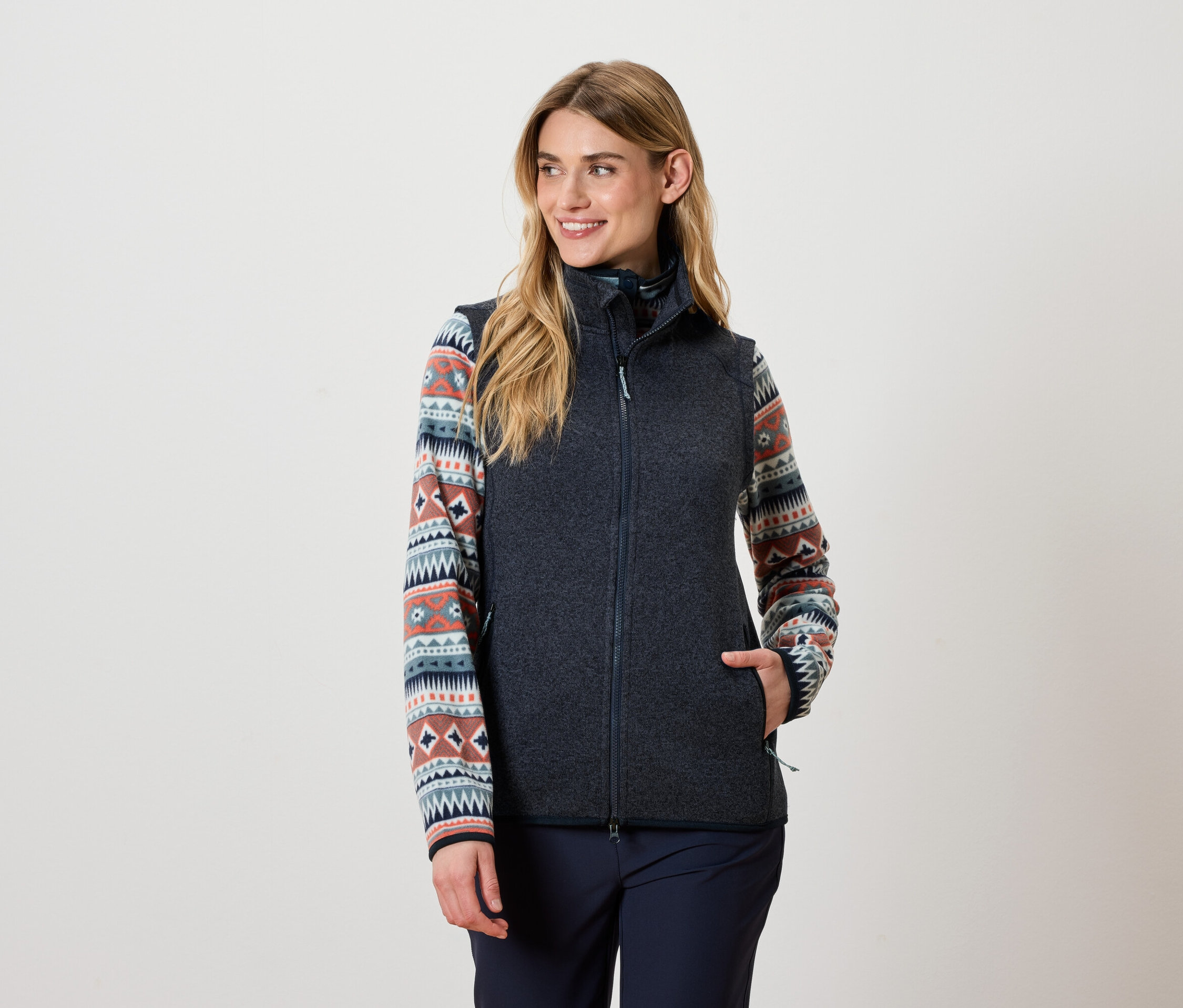 Frau trägt eine dunkelgraue Weste und ein gemustertes Oberteil.