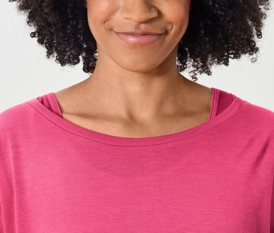 Oberkörper einer lächelnden Frau mit dunklen lockigen Haaren in einem pinkfarbenen T-Shirt.