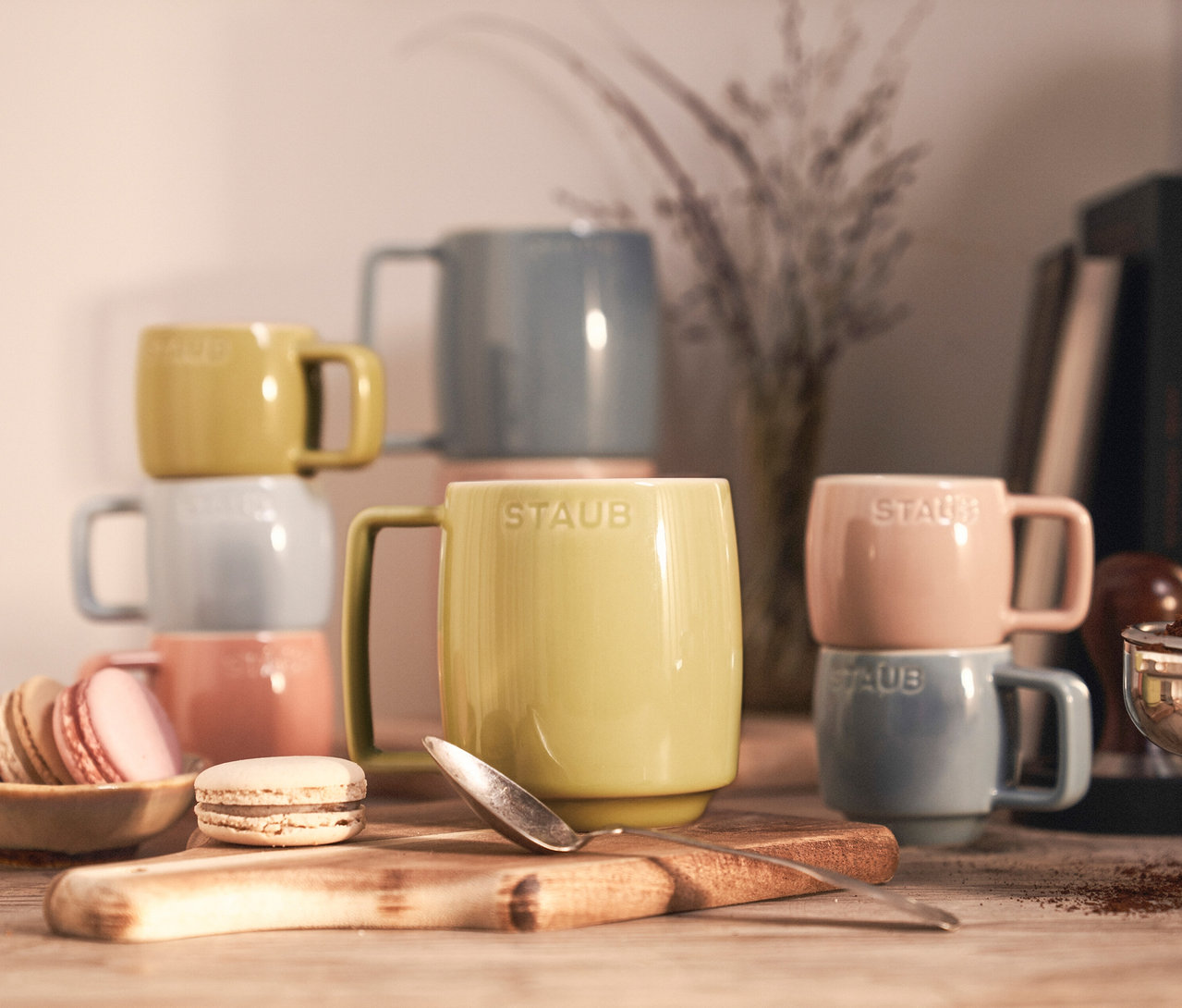 Verschiedenfarbige 6 STAUB Espressotassen »Macaron« und 6 STAUB Kaffeebecher »Macaron« stehen gestapelt auf einem Holztisch.