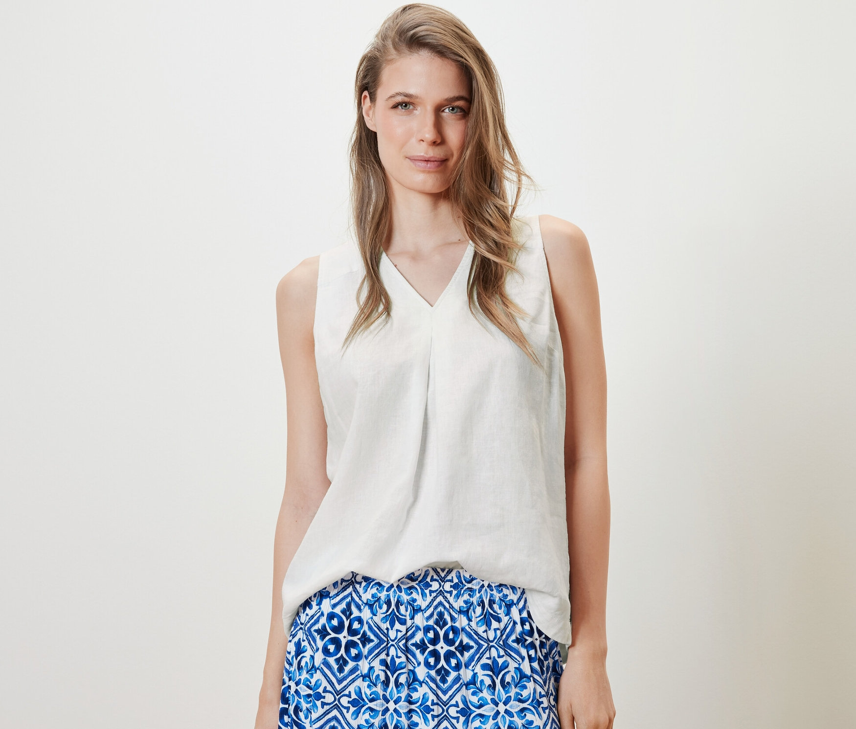 Frau trägt ärmellose Leinenbluse, weiß, und einen blauen Rock.