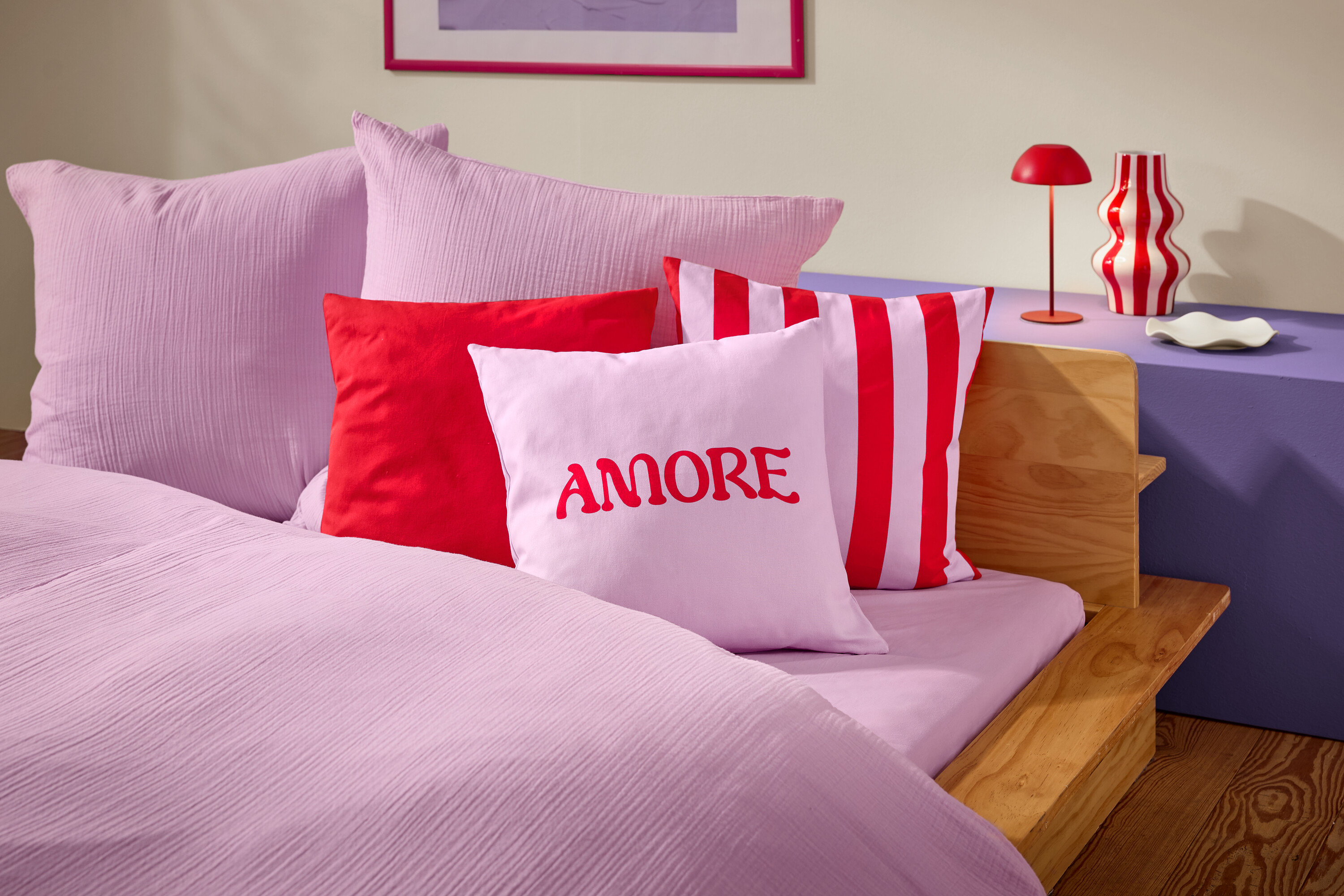 Nahaufnahme eines Bettes mit rosa Bettwäsche und Kissen. Ein Kissen hat das Wort AMORE in roter Schrift.