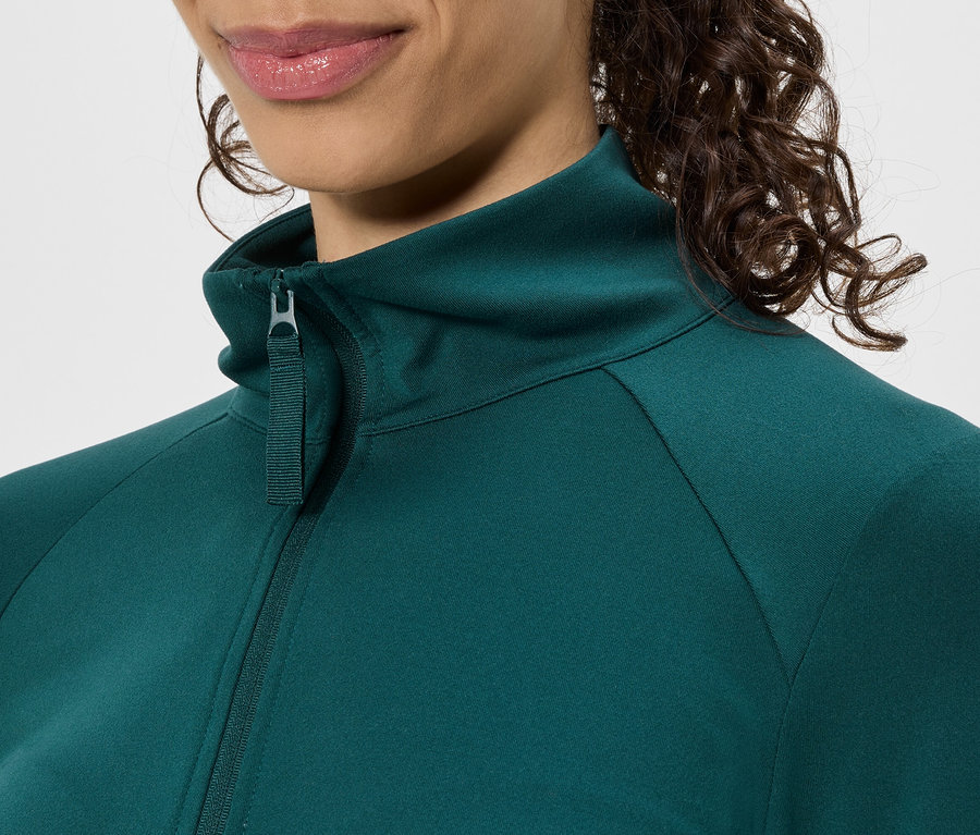 Nahaufnahme einer Frau, die eine grüne Jacke mit Reißverschluss und Stehkragen trägt.