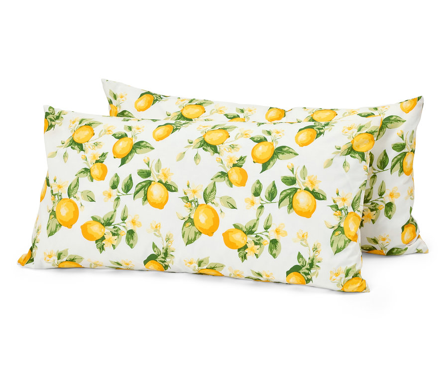 Zwei weiße Kissen mit einem Muster aus Zitronen, Blättern und Blüten liegen übereinander.