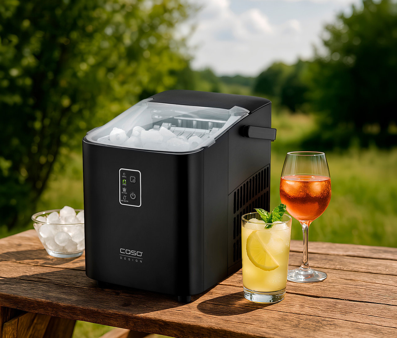 IceChef Compact Eiswürfelbereiter neben zwei Gläsern mit Getränken und einer Schale mit Eiswürfeln auf einem Holztisch im Freien.
