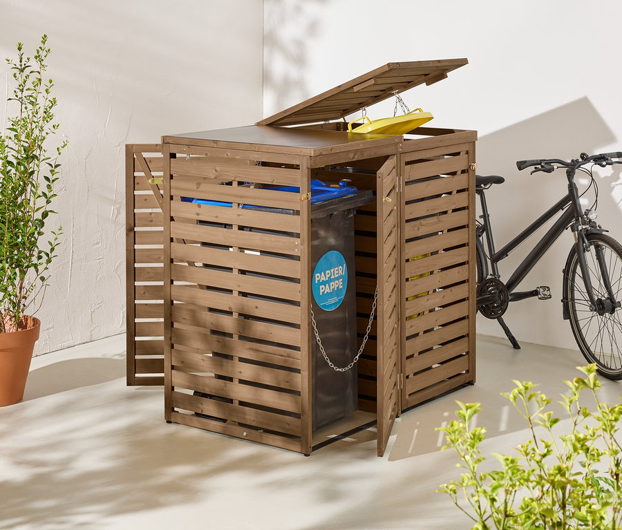 Eine braune Mülltonnenbox aus Holz mit geöffneten Türen und Deckel steht neben einem schwarzen Fahrrad.