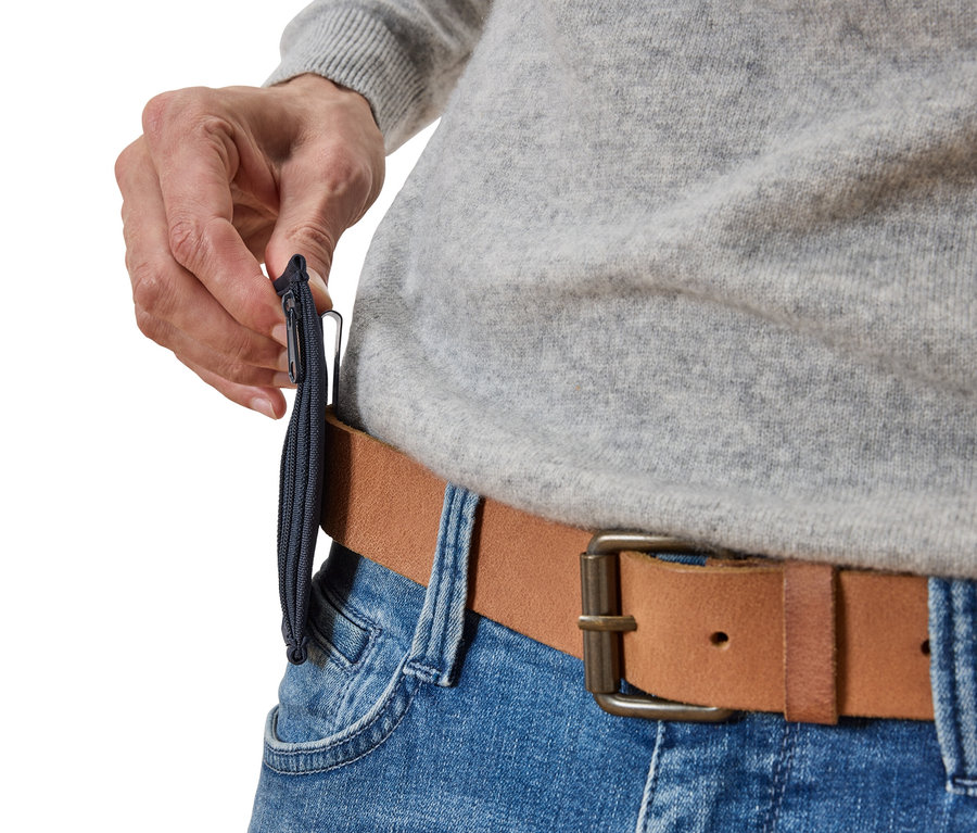 Nahaufnahme einer Person, die eine schmale, marineblaue Reißverschlusstasche an einem braunen Ledergürtel befestigt, getragen über blauen Jeans.