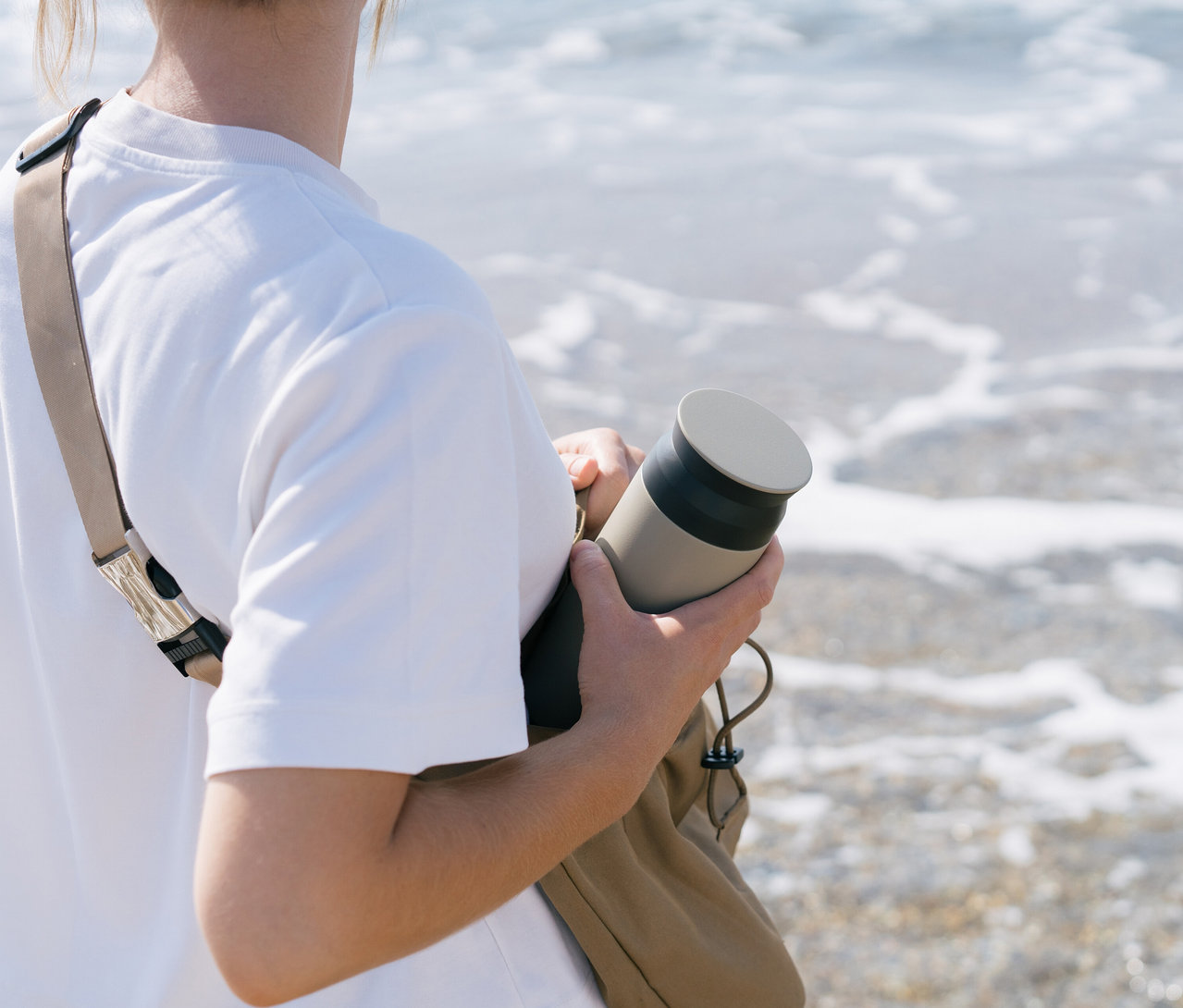 Eine Person hält eine beigefarbene Flasche in der Hand, während sie am Strand steht.