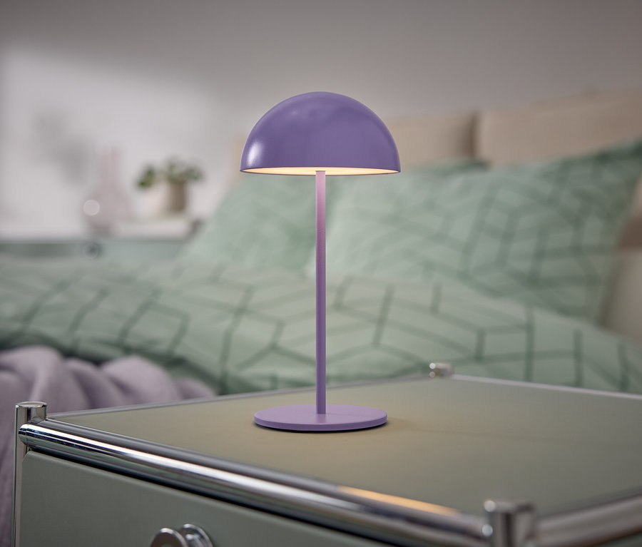 Eine lila Lampe steht auf einem Nachttisch neben einem Bett.